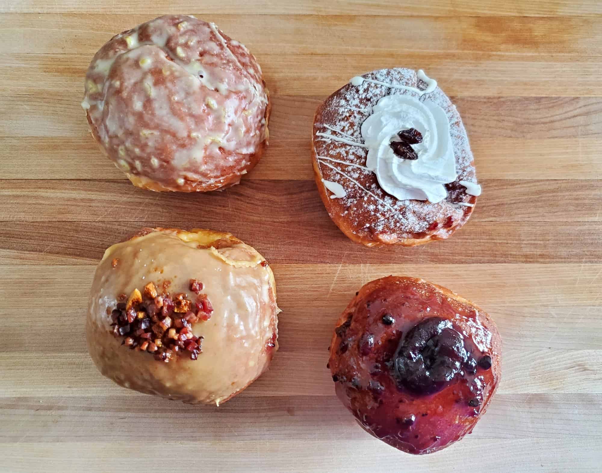 Four gorgeous paczki from Kolateks Bakery sitting on a wooden cutting board, shot from overhead.