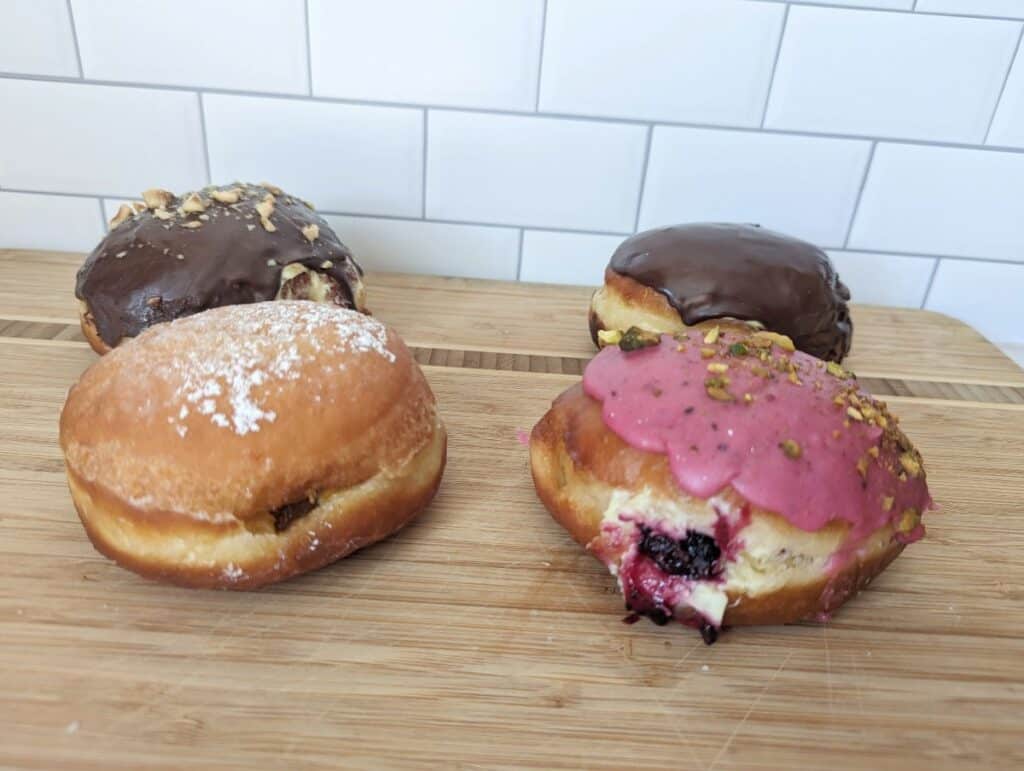 Four paczki on a board from Sweet Generations sitting on a wooden board.