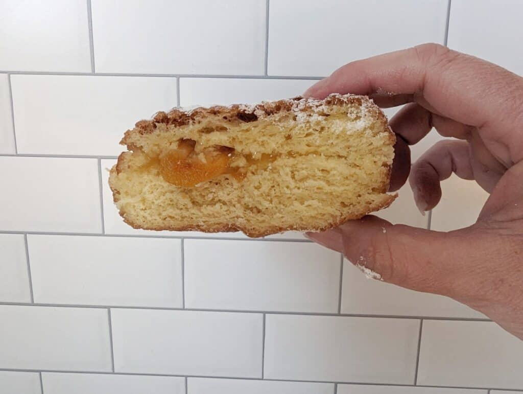 Poorly filled apricot paczek from Country Style Donuts held by a hand in front of subway tile.
