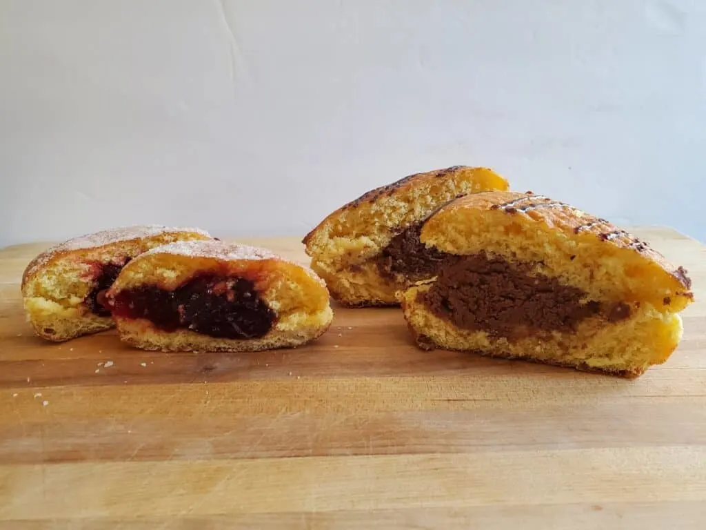 Raspberry and chocolate paczki from Beth's Little Bake Shop cut in half sitting on a wooden board.