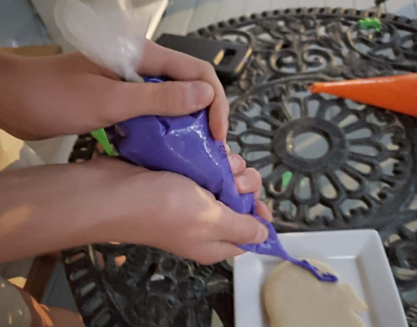 Holding a purple bag of icing to decorate a cookie