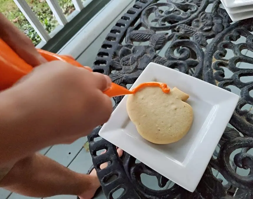 Outlining a pumpkin cookie in orange frosting