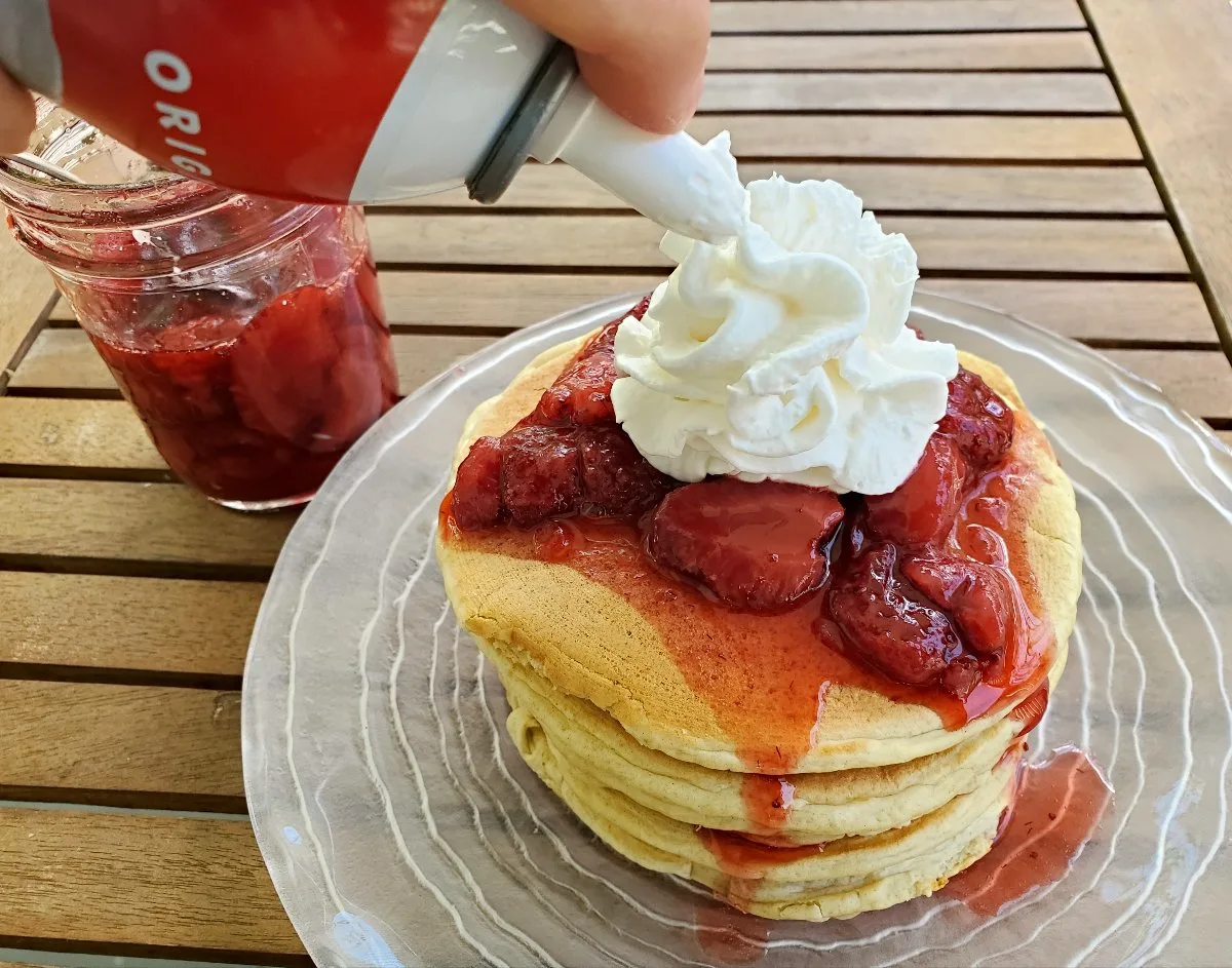 Adding whipped cream to a pancake stack