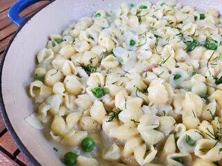 Closeup of a pot of pasta with peas and fresh dill.