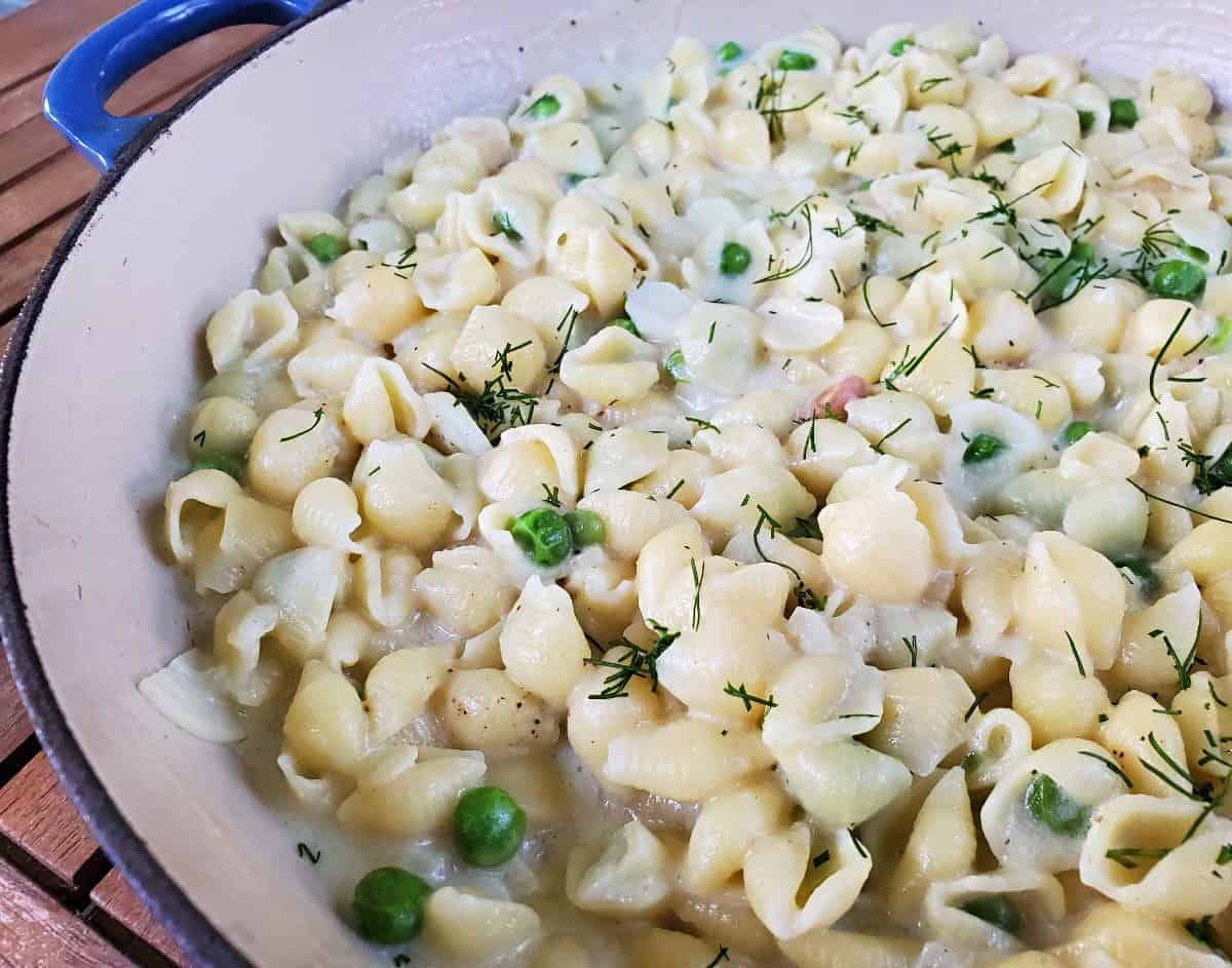 Closeup of a pot of pasta with peas and fresh dill.