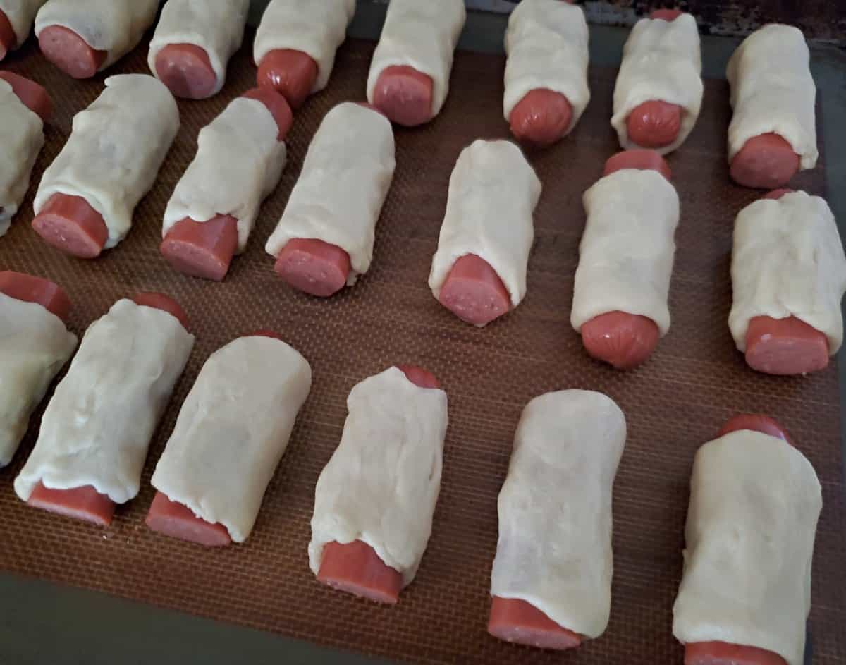 Silpat with three row of unbaked bagel dogs.