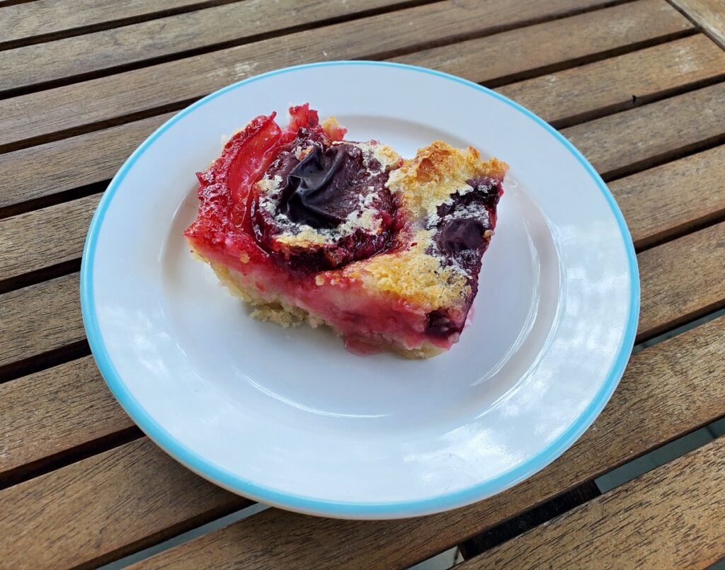 Slice of homemade peach kuchen on a plate on a wooden table.