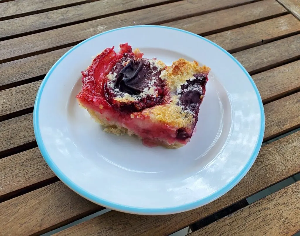 Slice of homemade peach kuchen on a plate on a wooden table.