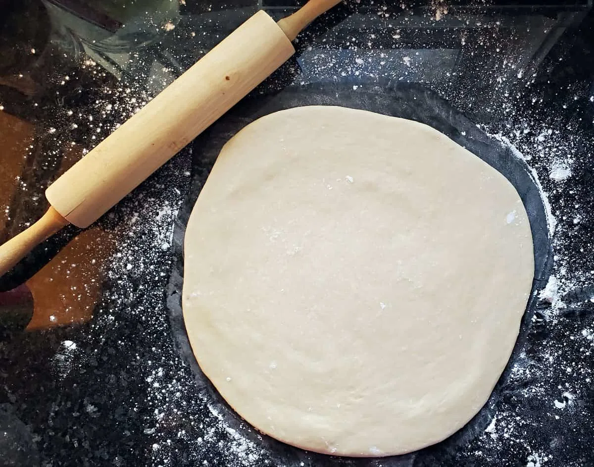 12 inch round of dough next to a rolling pin.