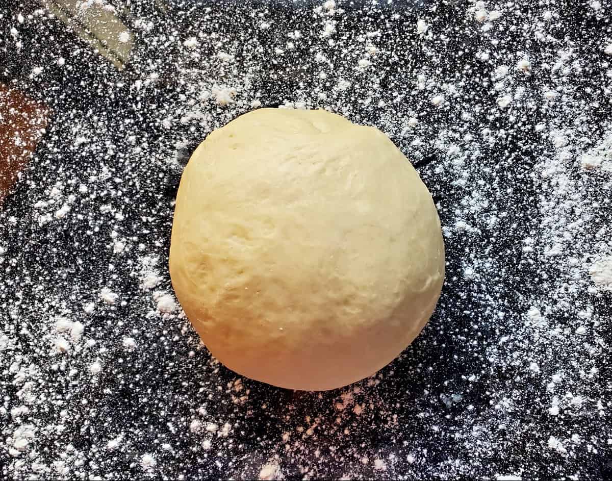 Ball of crescent roll dough on lightly floured black counter.