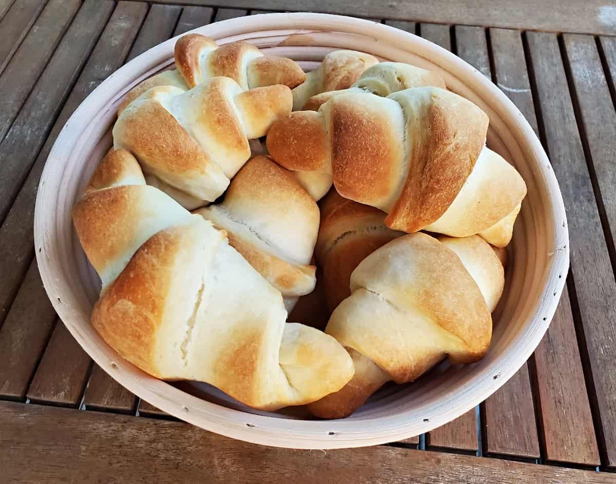 Basket of golden brown crescent rolls on a wooden table.