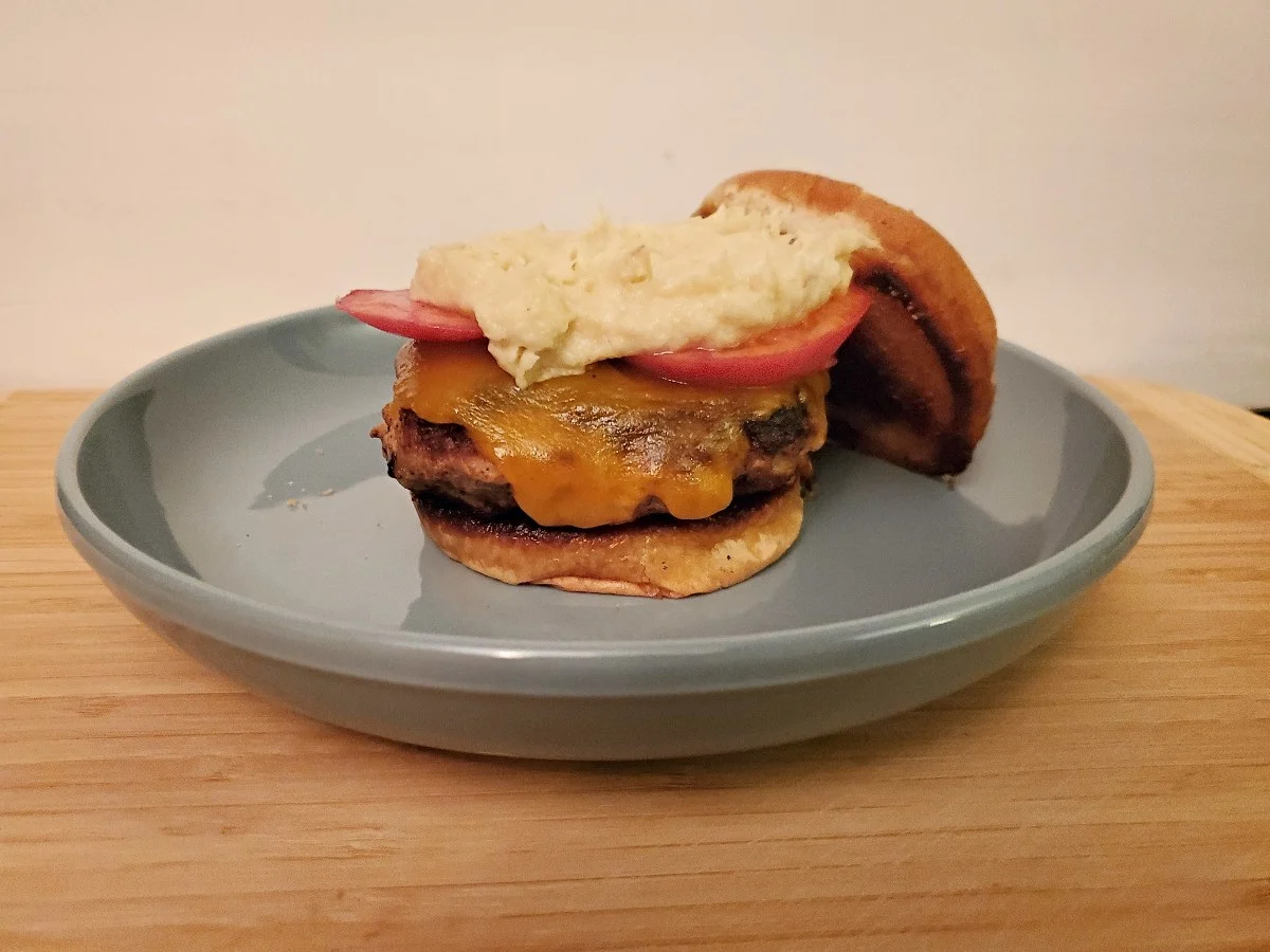 Asian turkey burger on a plate with tomatoes cheese and parsnip puree.