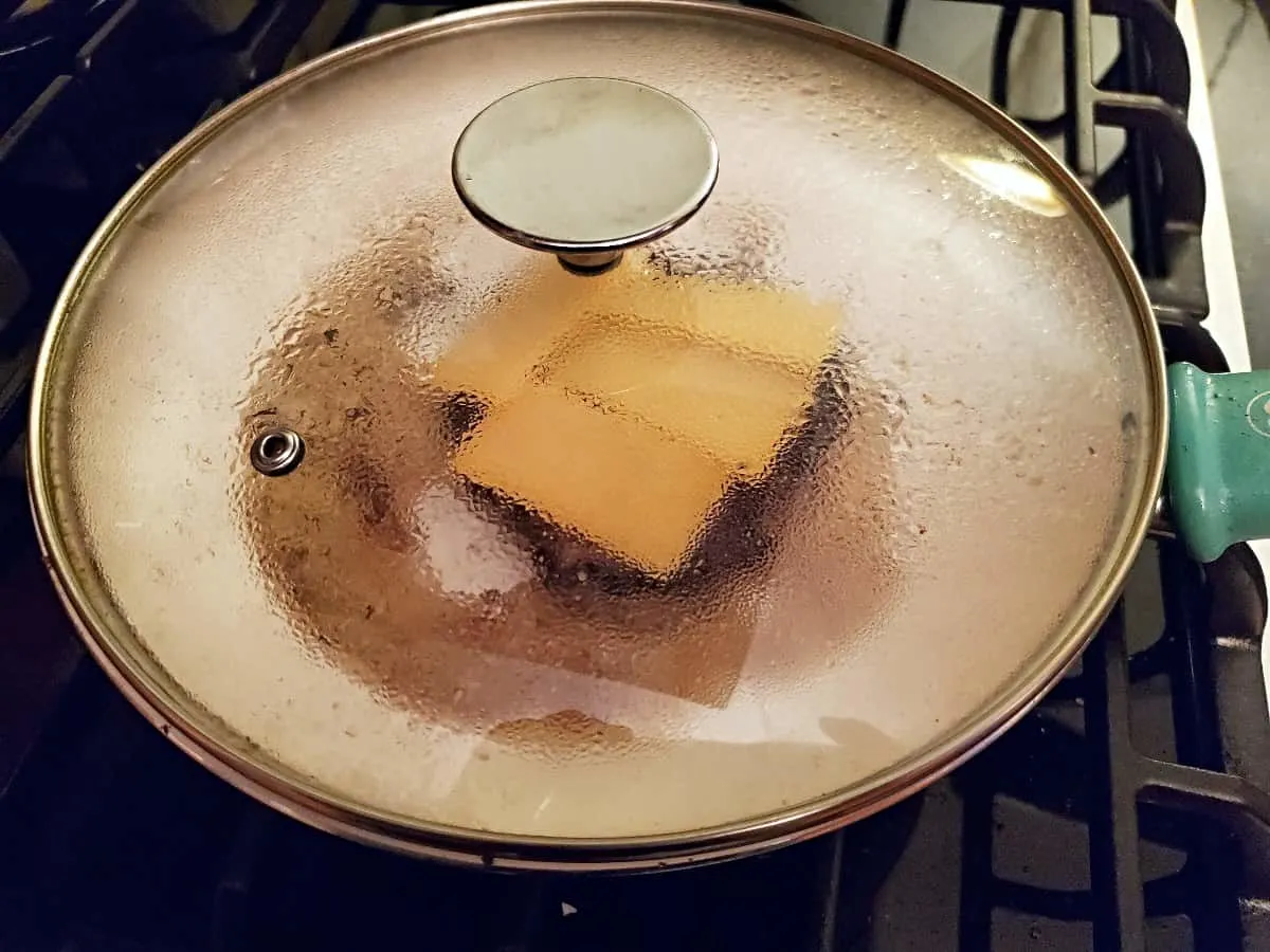 Asian turkey burgers with cheese and a lid on the pan to help cheese melt.