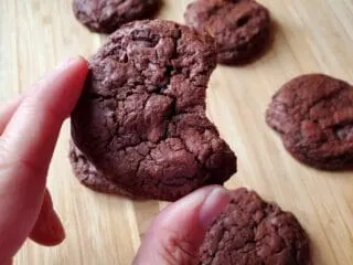 Fingers holding a chocolate cookie with a bite taken out over other cookies.