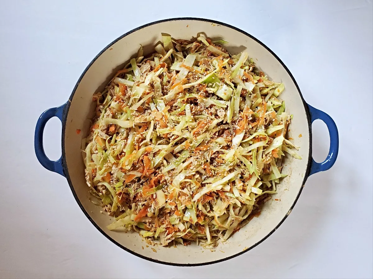 Overhead view of a large cast iron skillet with chicken egg roll in a bowl.