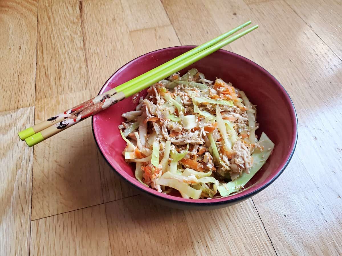 Three quarter view of deconstructed chicken egg roll in a red bowl with chopsticks resting on top.
