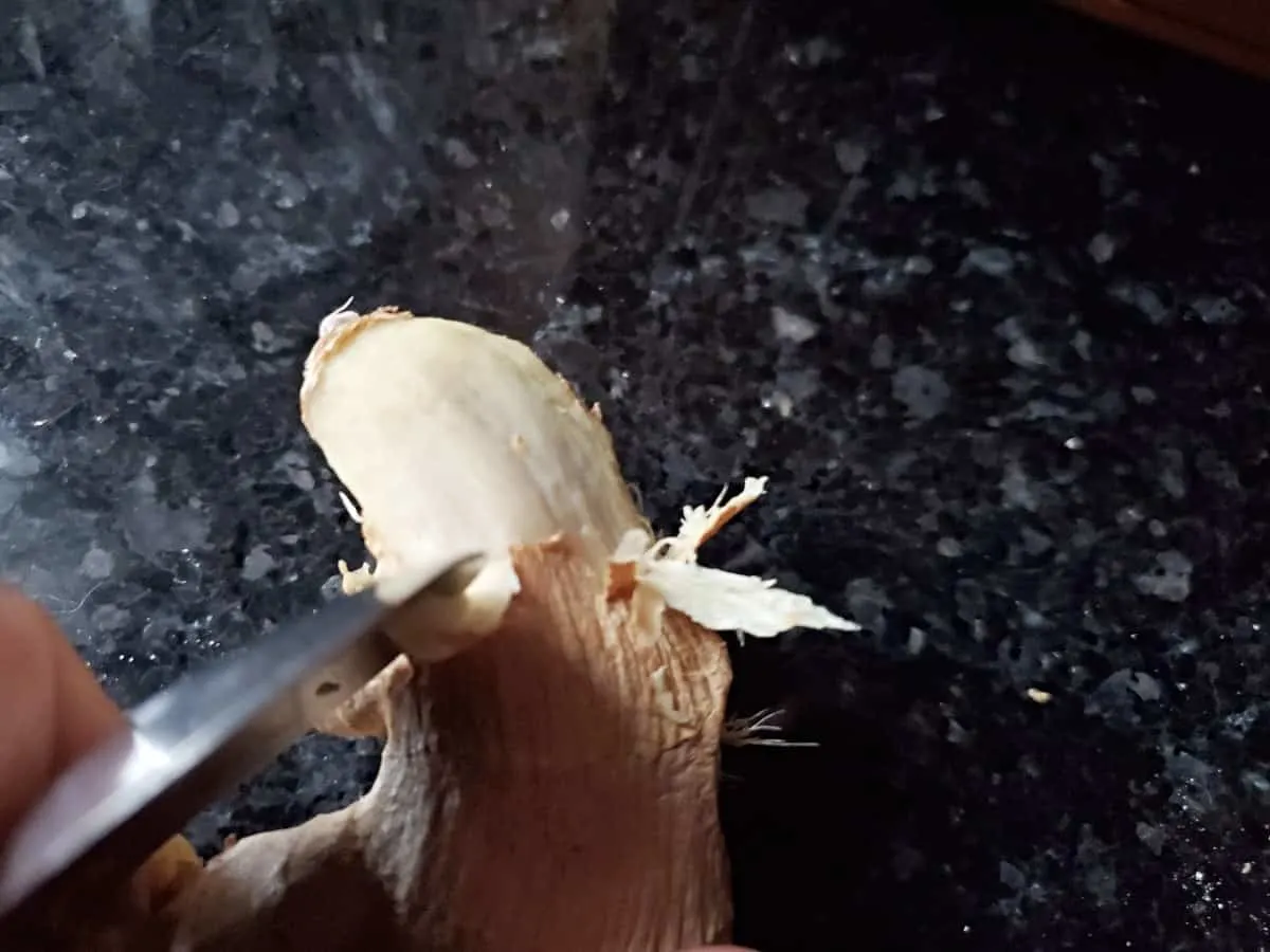 Using the side of a spoon to scrape off ginger skin.