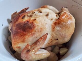 Side angle of a lemon roast chicken in a white dutch oven.