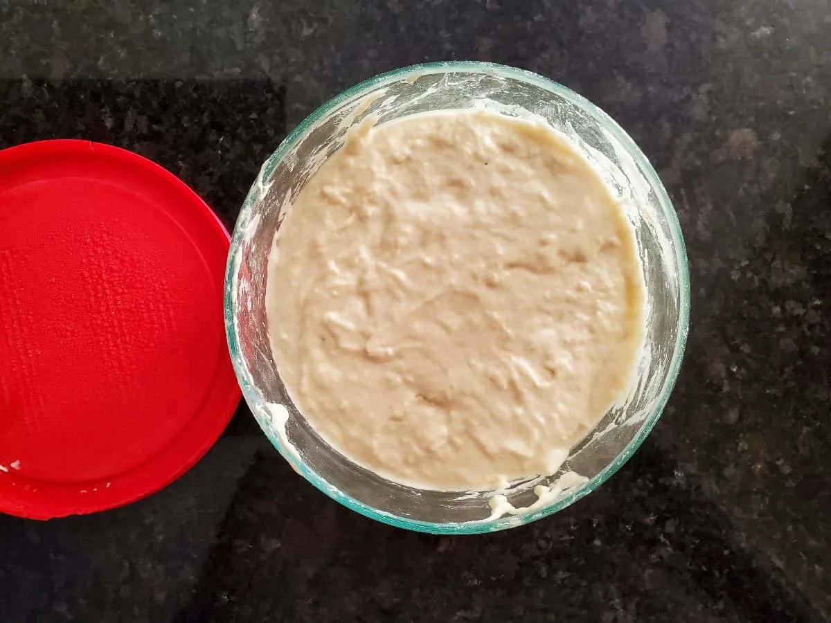 Sourdough sponge for bread bowls in a glass bowl on a black counter.