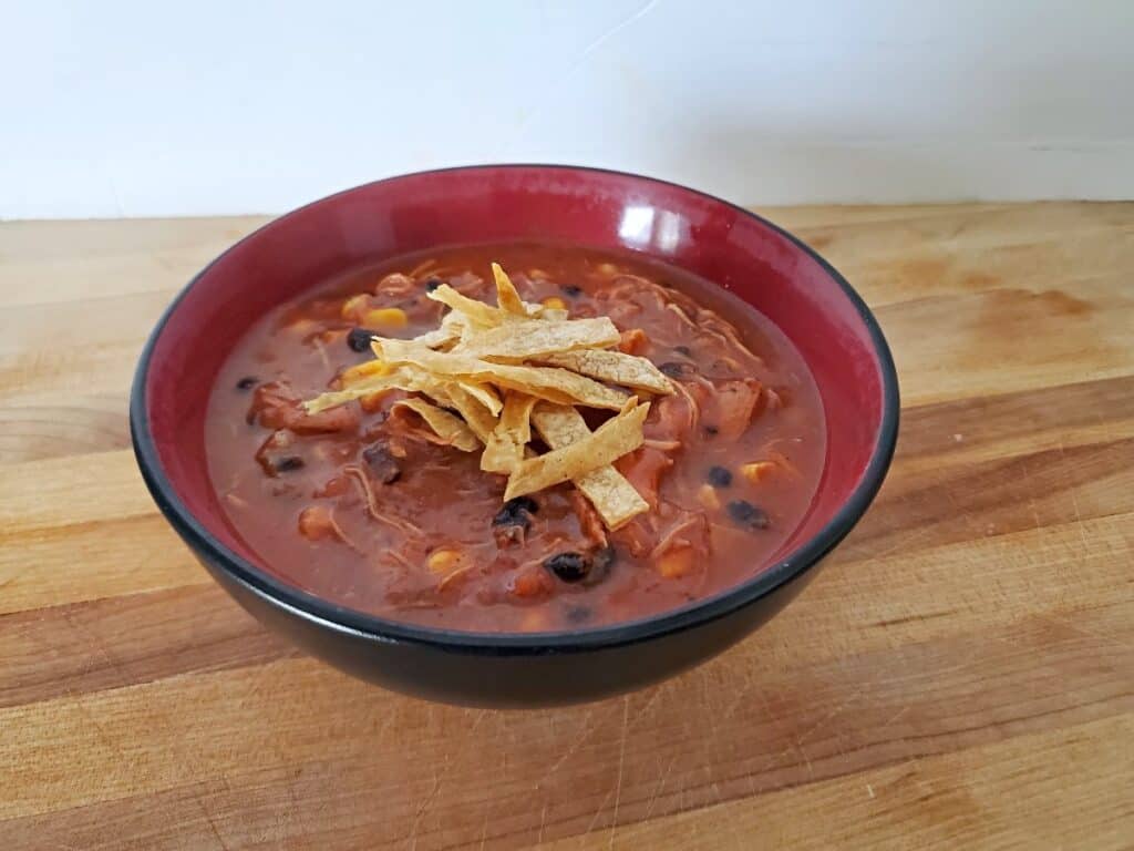 Bowl of chicken tortilla soup with tortilla strips on a wooden background.