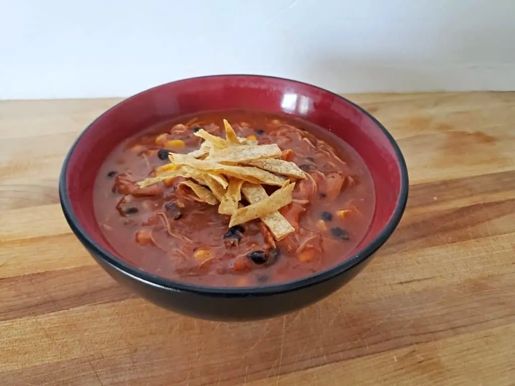 Bowl of chicken tortilla soup with tortilla strips on a wooden background.