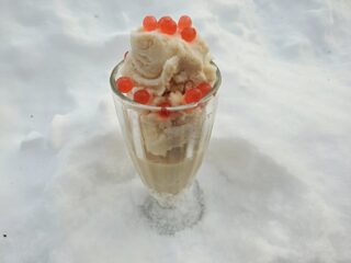 Glass with brown sugar snow cream sitting in snow and topped with boba.