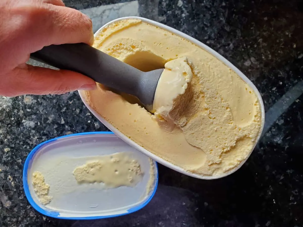 Overhead shot showing a hand scooping vanilla ice cream from a container.