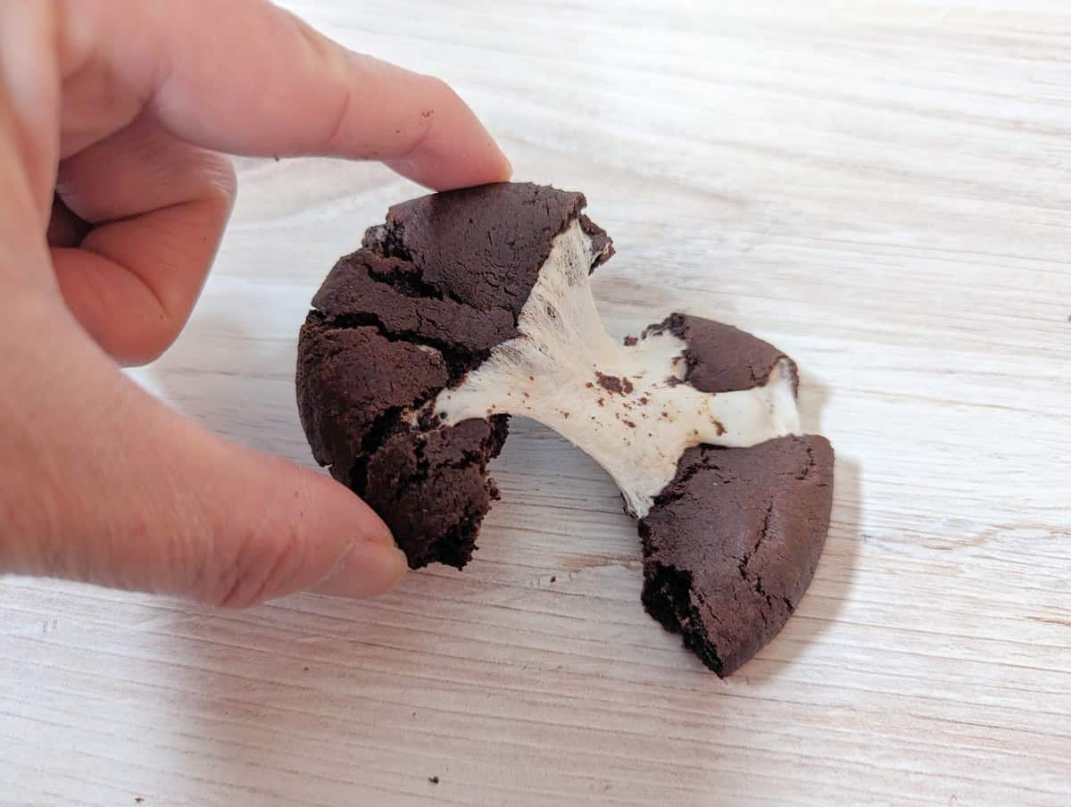 Image shows a Chocolate Marshmallow Cookie being pulled apart on a wooden table.