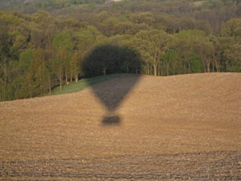 Hot air balloon shadow across an empty field.