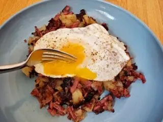 Fork cutting into a runny egg over corned beef hash.