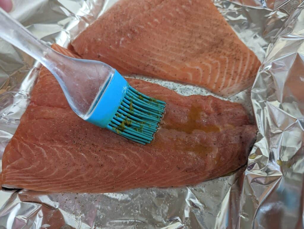 Pastry brush adding glaze to raw salmon in foil.