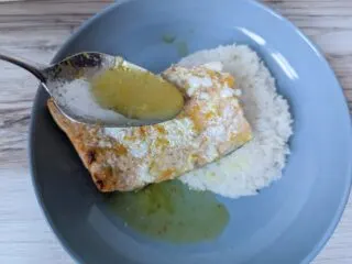 Spoon drizzling orange glaze on salmon with rice on a blue plate.