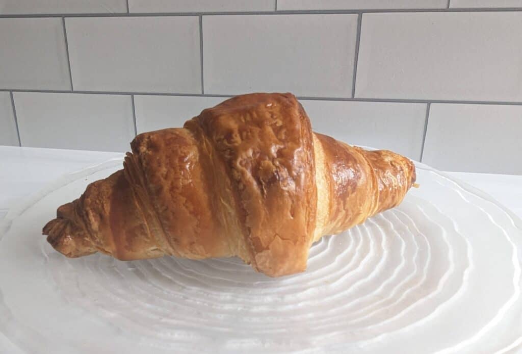 Baked croissant sitting on a clear round plate.