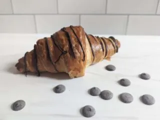 Chocolate drizzled croissant on a white background with chips around it.