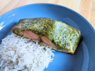 Image shows Three quarters view of pesto salmon with rice on a blue plate.