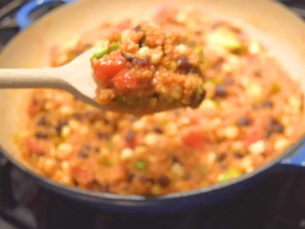 Image shows a wooden spoon holding a scoop of Mexican skillet quinoa with the full pot behind it.