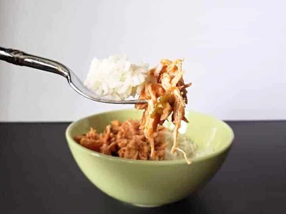 Image shows a Bite of tomato lime chicken on a fork with rice and the rest of the bowl in the background.