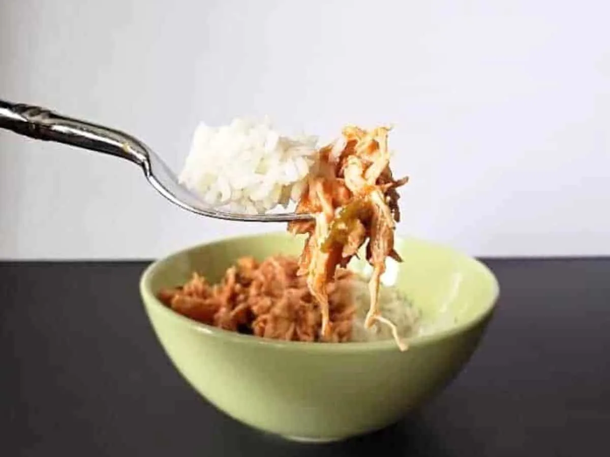 Image shows a Bite of tomato lime chicken on a fork with rice and the rest of the bowl in the background.