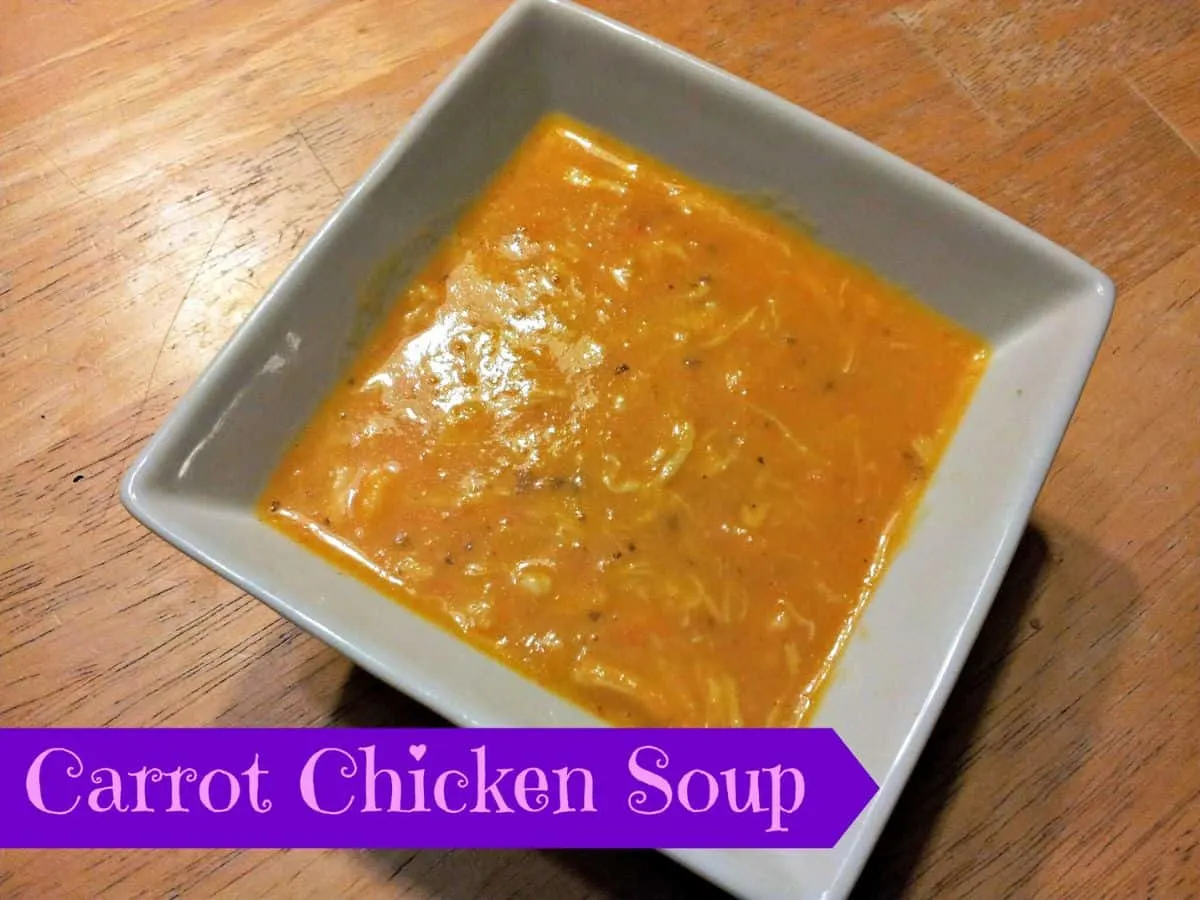 Image shows A bowl of carrot chicken soup on a wooden table.