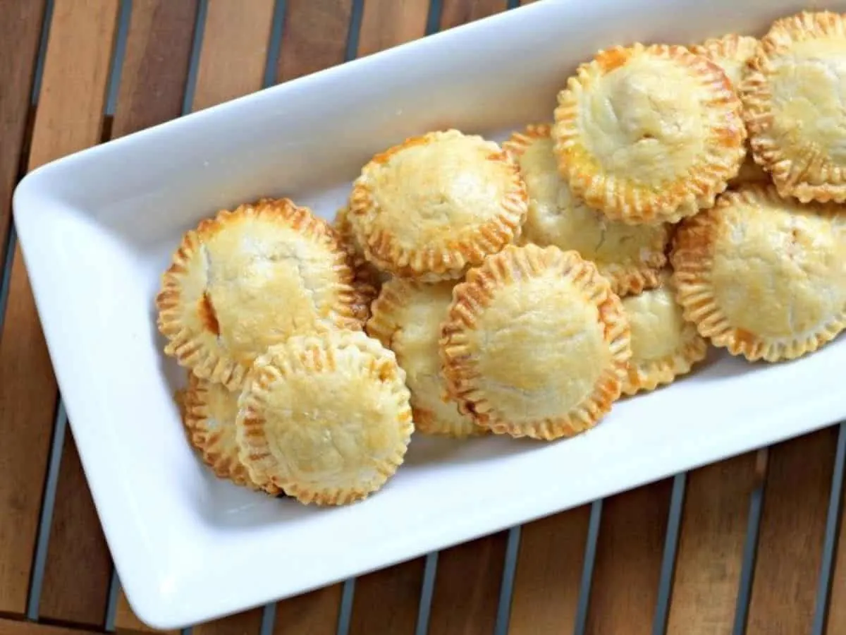 Image shows an overhead shot of puff pastry Chicken Empanadas on a white tray.