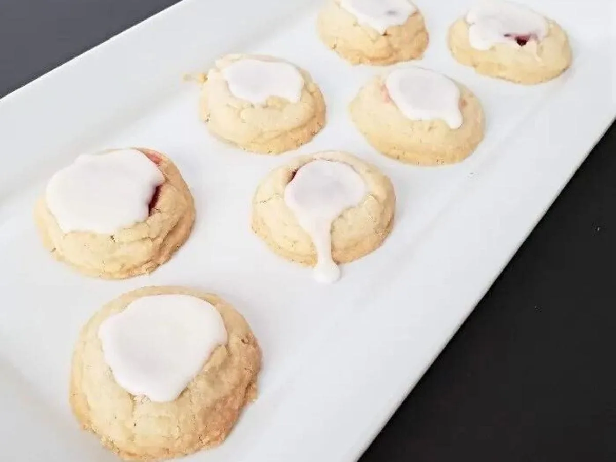 Hand holding a thumbprint cookie with a bite taken out of it over a tray filled with more classic thumbprint cookies.