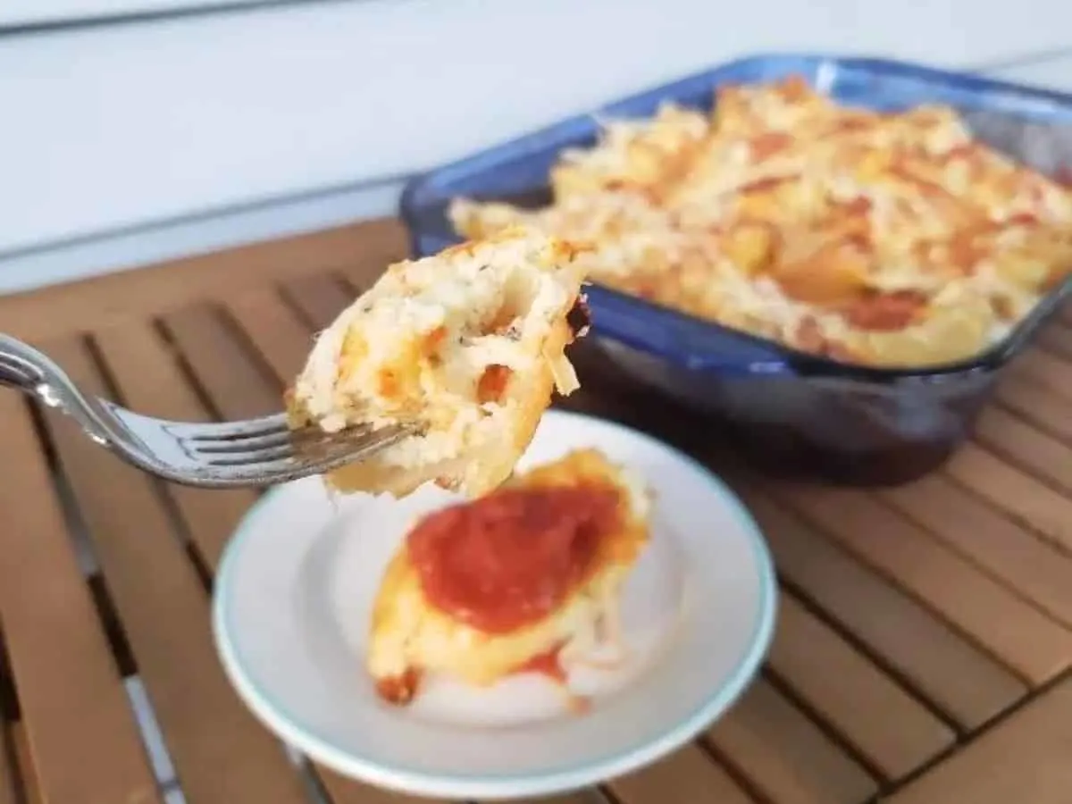 Image shows an overhead shot of Easy Cheesy Stuffed Shells with a small plate holding one and the rest of the pan next to it.