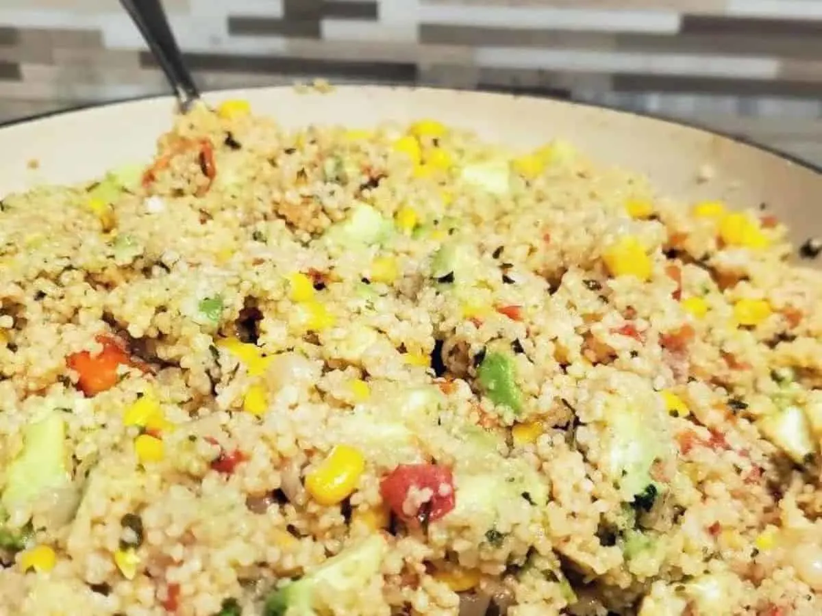 Image shows a closeup of an enameled cast iron pan filled with a vegan couscous salad.