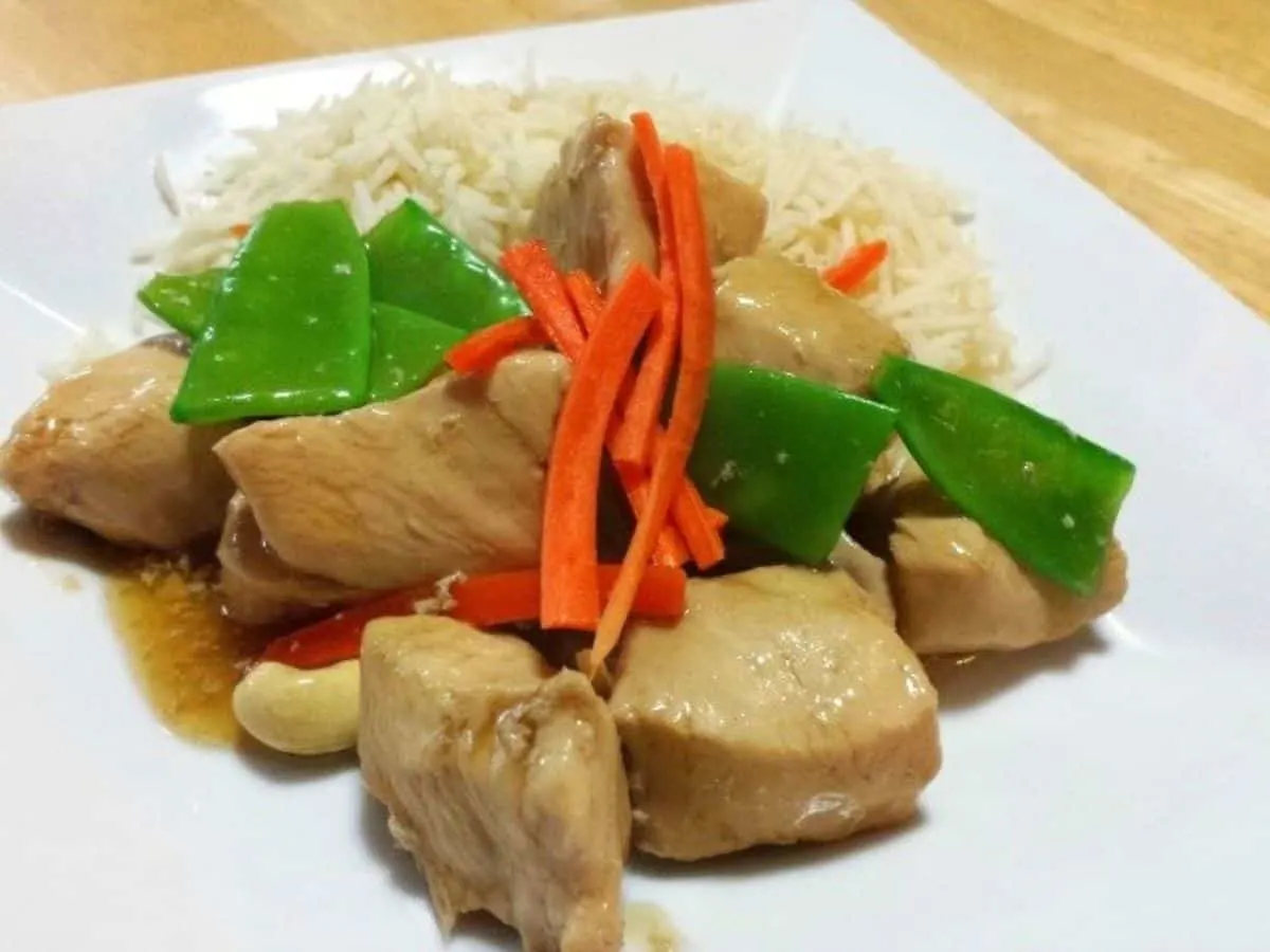 Image shows Cashew chicken on a white plate garnished with carrots and snow peas.