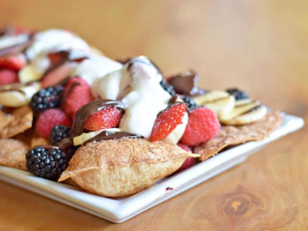 Image shows dessert nachos on a plate topped with fruit and whipped cream.