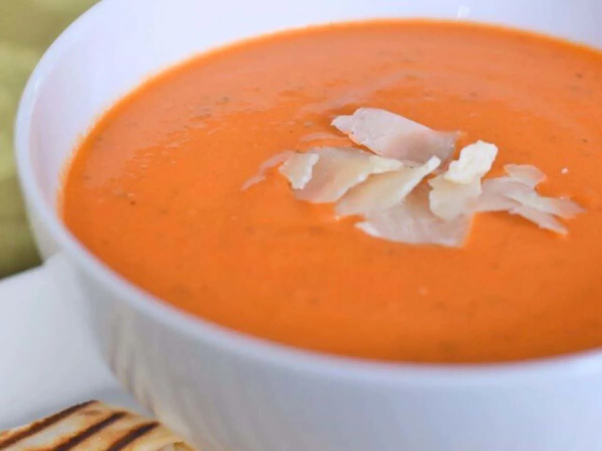 Image shows a close up of a bowl of Tomato Basil Bisque with grated parmesan on top of it.