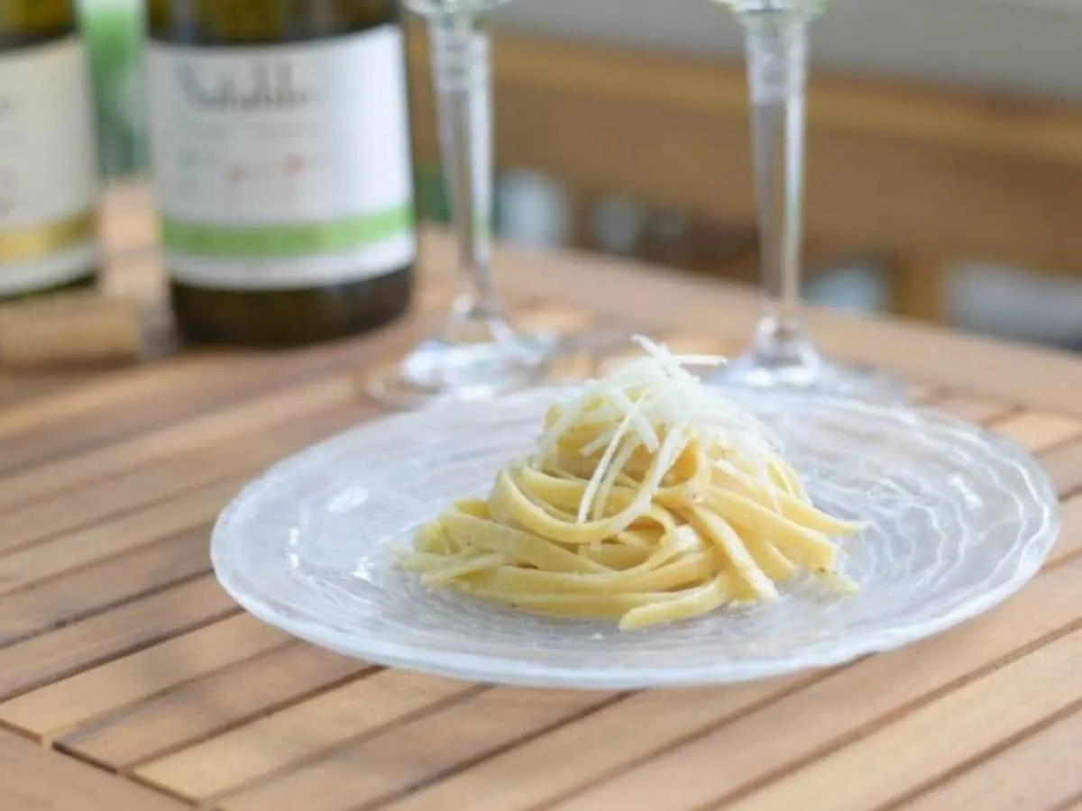 Image shows a plate with cacio e pepe in a neat pile topped with shaved parmesan cheese.