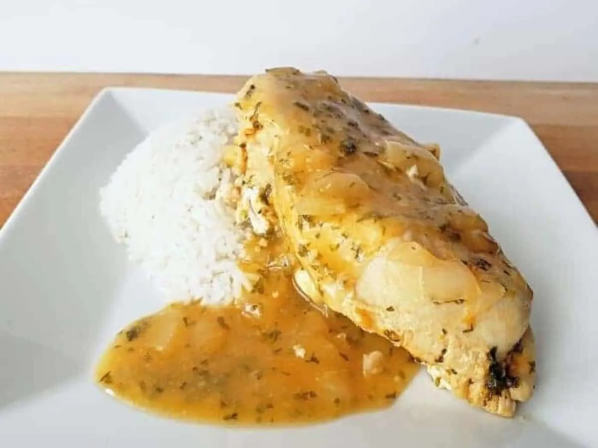 Close up image of lemon garlic chicken with rice on a white plate.