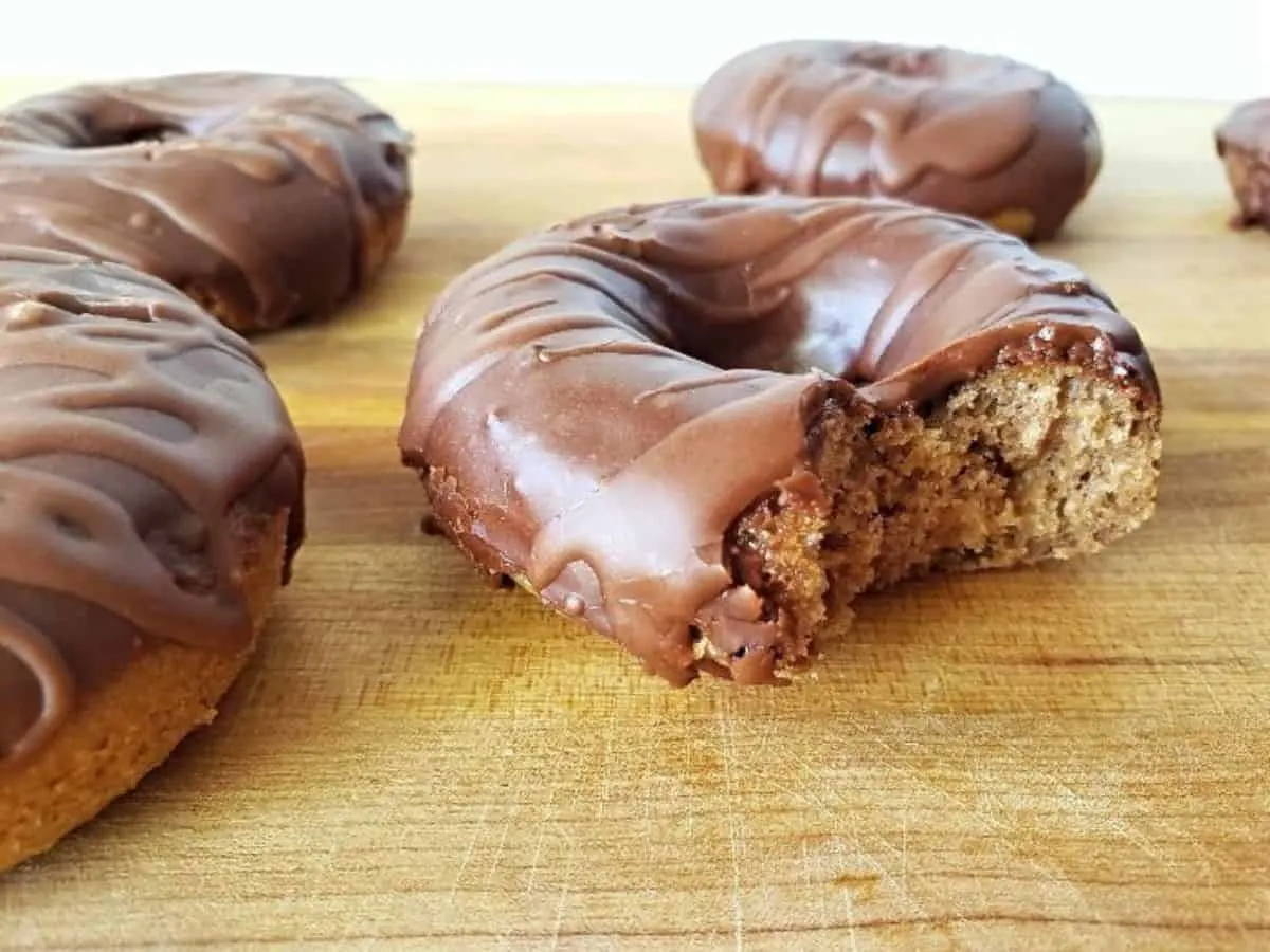 Image shows Mocha donuts on a wooden board with one missing a bite.