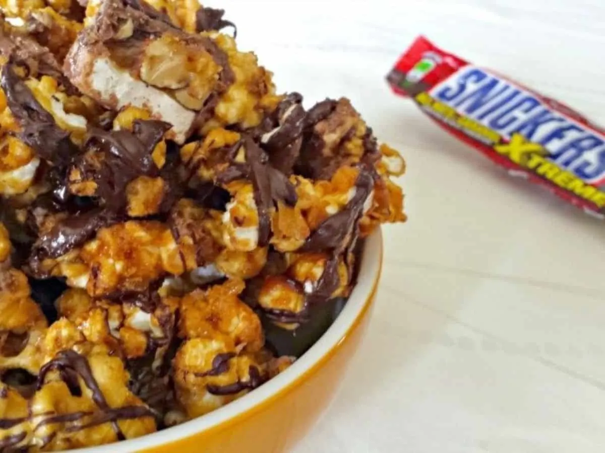 Image shows a bowl with Snickers Popcorn next to a Snicker's bar.